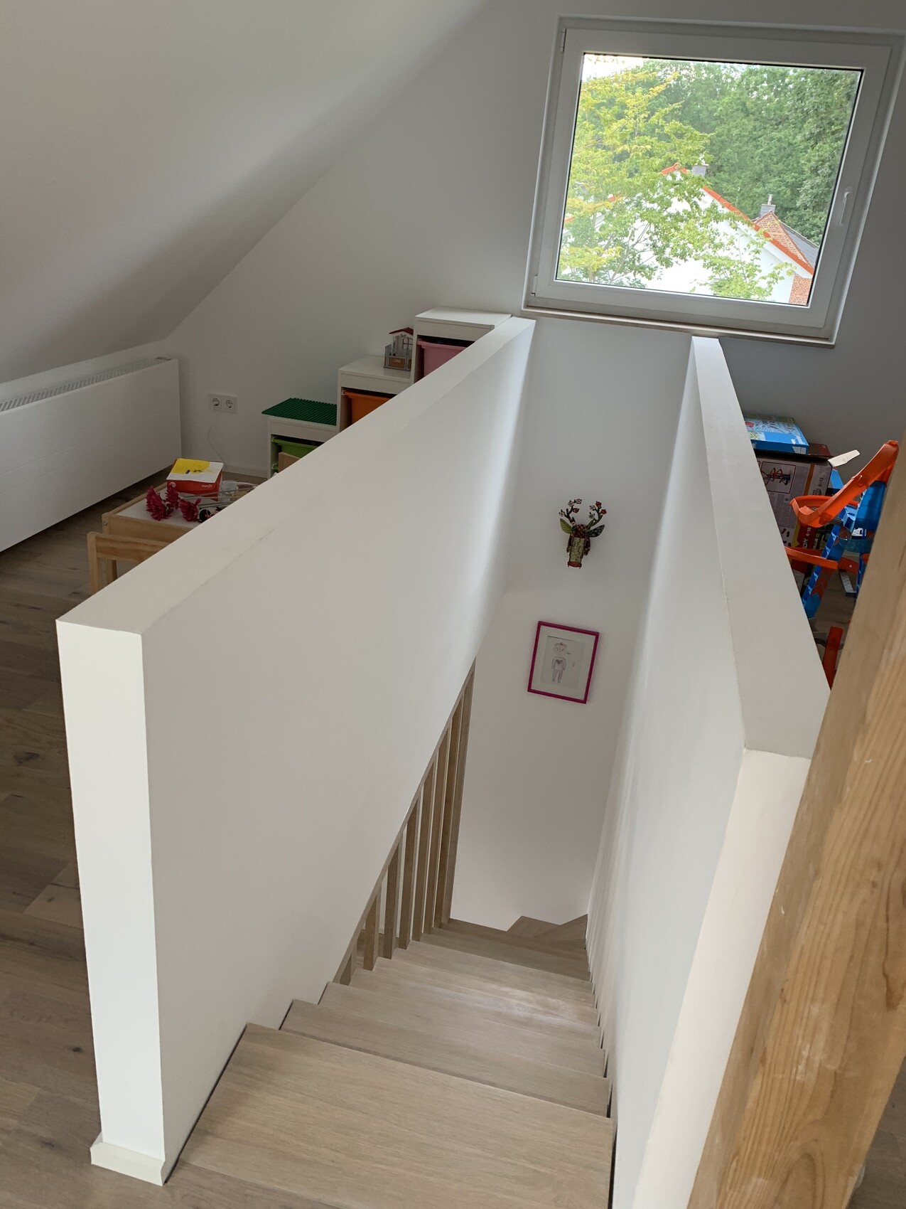 Weißer Treppenaufgang im Dachgeschoss, Blick in Spielzimmer mit Fenster und Baum draußen.