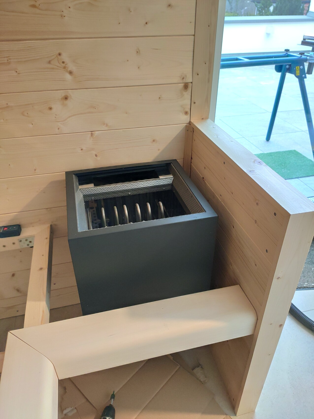 Kleiner Heizofen in einem Holzraum, Metallgehäuse und Rostgitter sichtbar.