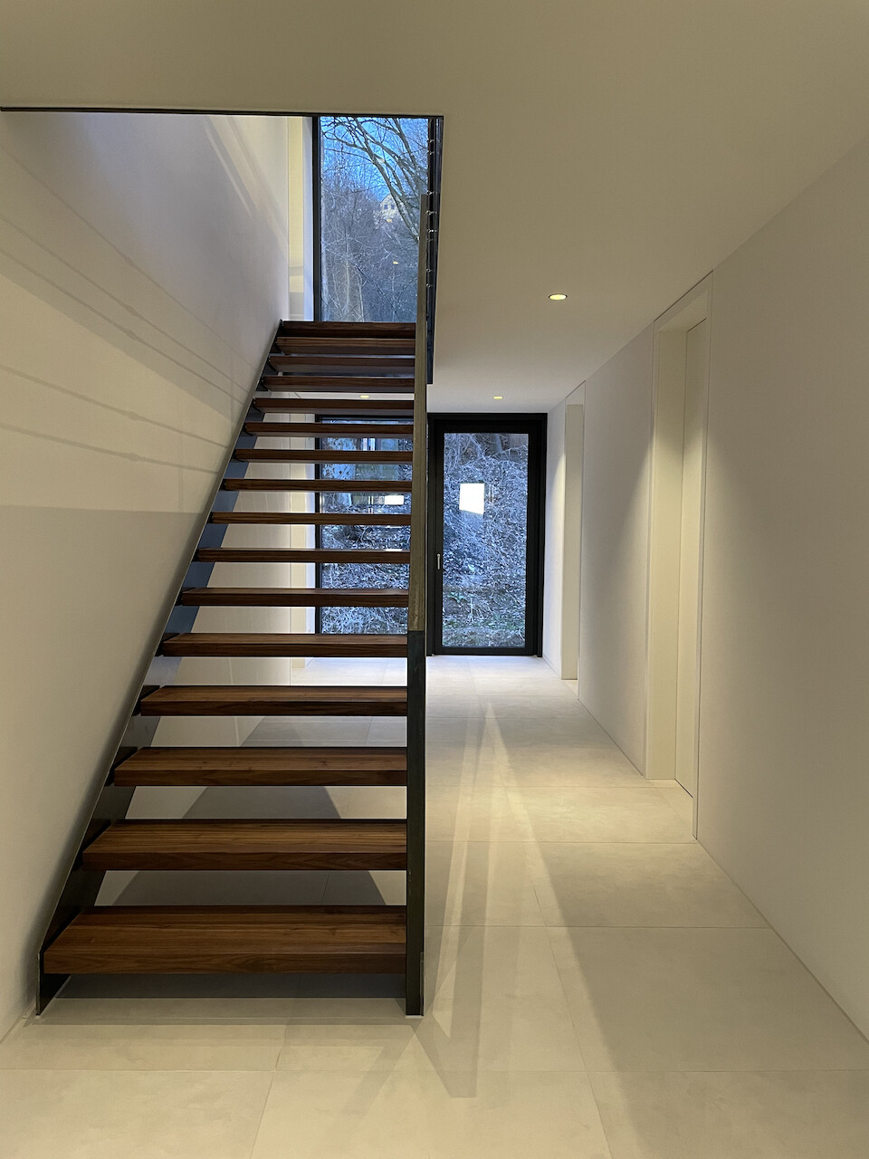 Moderne offene Holztreppe mit Metallrahmen, heller Flur, Glasfront am Ende