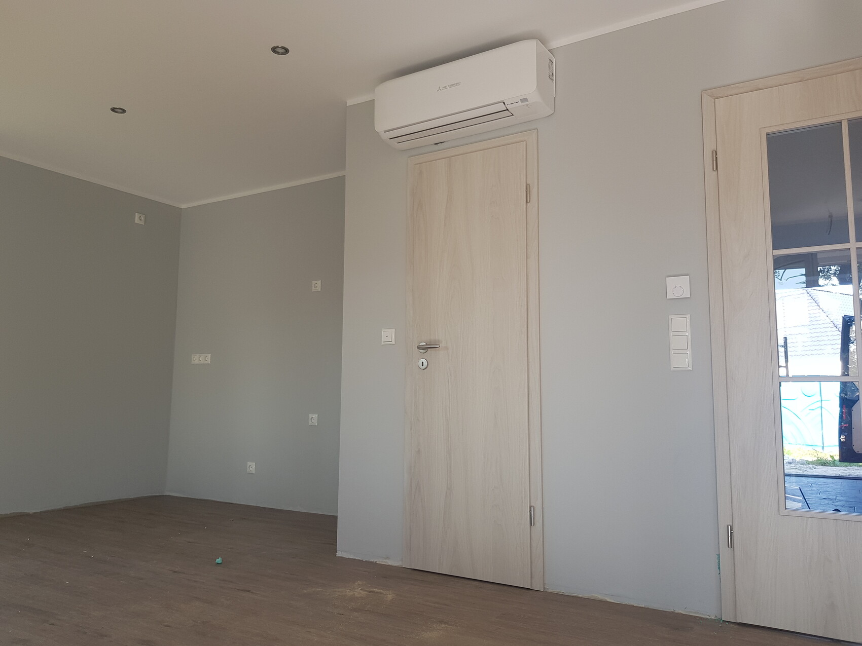 Heller Innenraum mit grauen Wänden, Holzfußboden, zentrale Holztür und rechts Glastür.