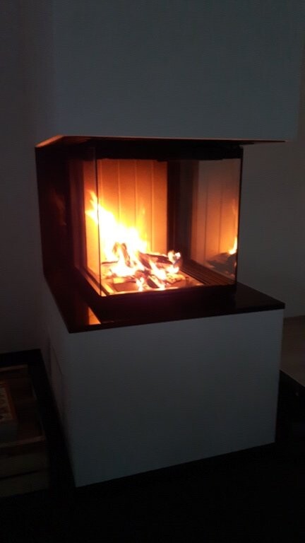 Moderne geschlossene Kamin-Feuerstelle mit brennenden Flammen hinter Glas auf weißem Podest.