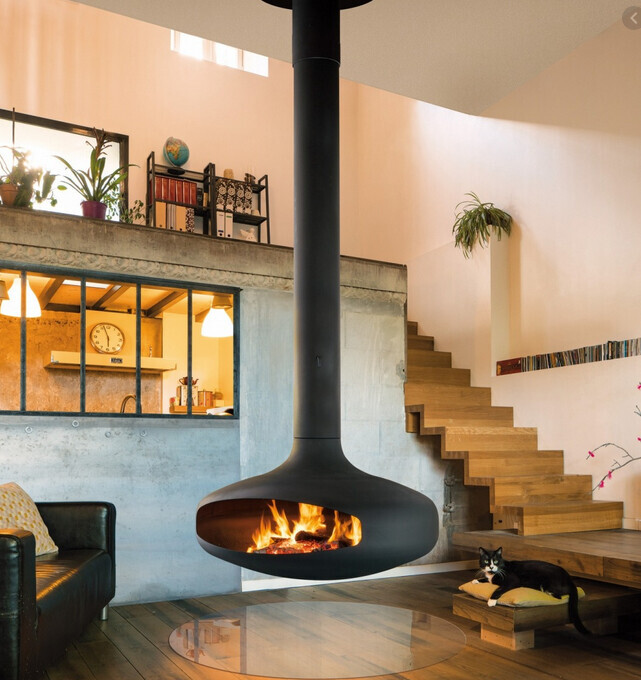 Moderner Wohnraum mit hängendem Kamin, Treppe, Sofa, Glas-Tisch und Katze auf Podest.