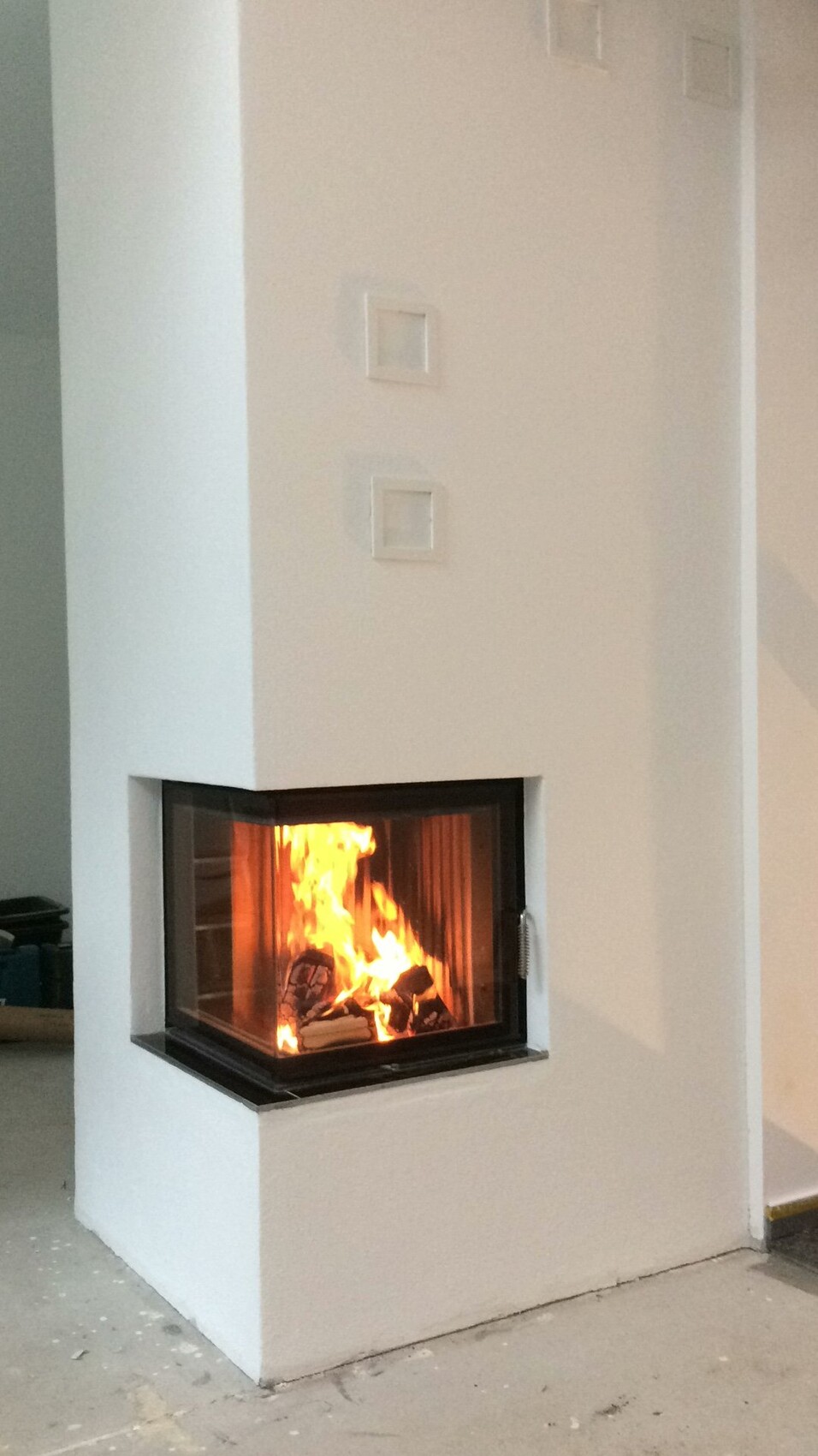 Weißer moderner Säulen-Kamin mit Glasfront und brennendem Holz.