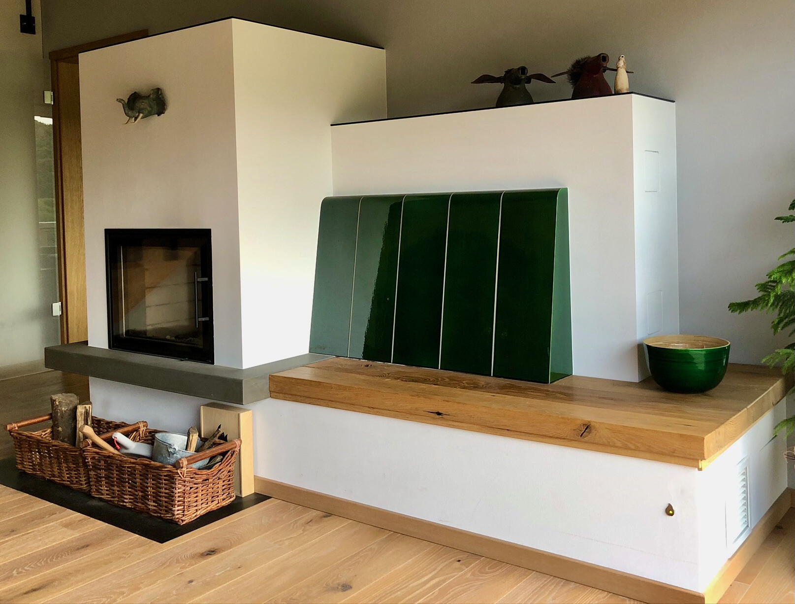 Moderner Wohnraum mit Kamin links, grüne Paneele vor weißer Wand, Holzboden und Korb Brennholz.