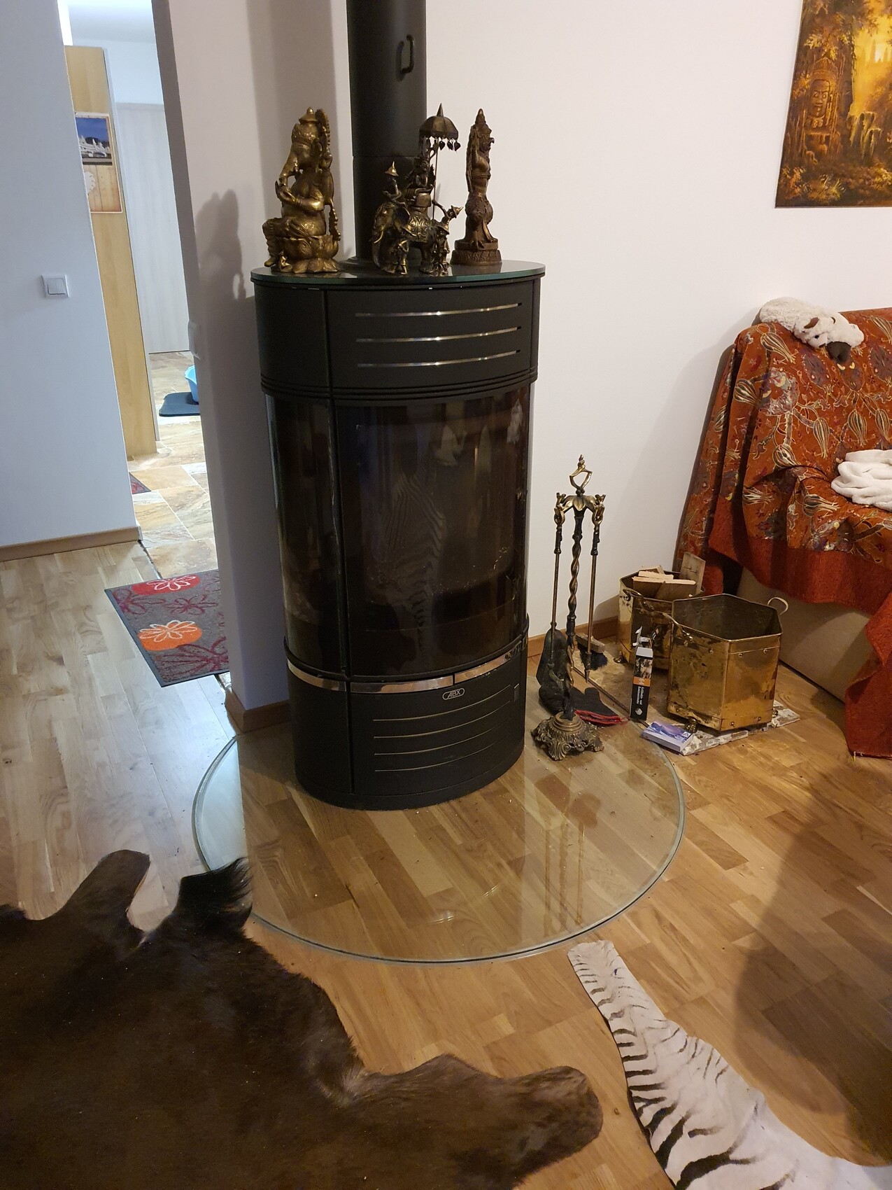 Schwarzer runder Kaminofen mit Glasfront; Statuen darauf. Daneben gemustertes Sofa im Wohnzimmer.