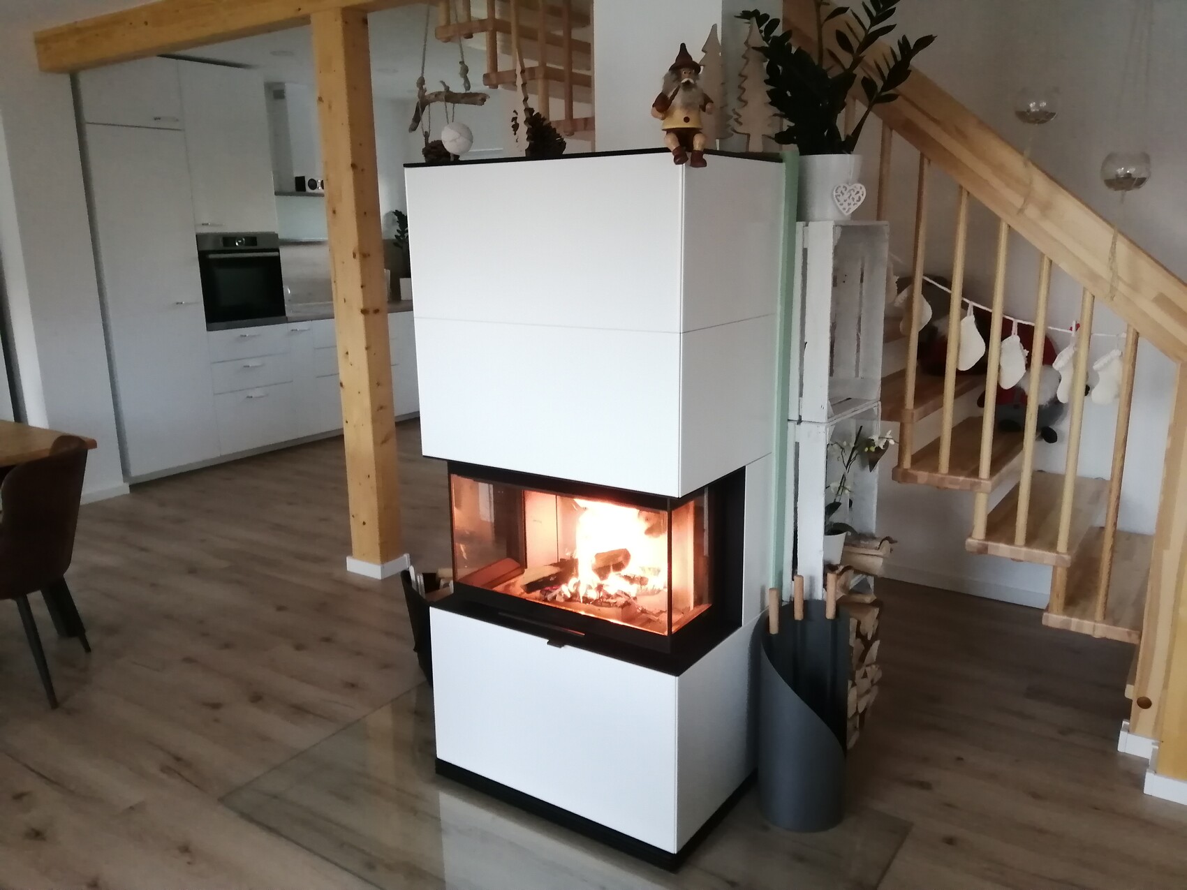 Moderne weiße Kaminofenanlage mit Glasfront brennendem Feuer im Wohnzimmer, Treppe rechts.