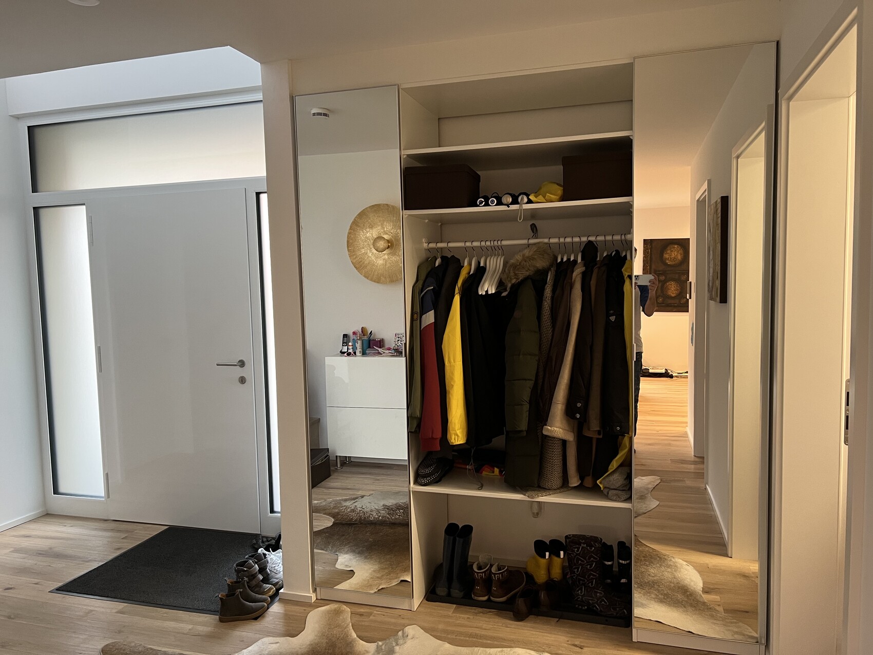 Offene Garderobe mit Mänteln und Schuhen; Spiegel, Fluransicht.