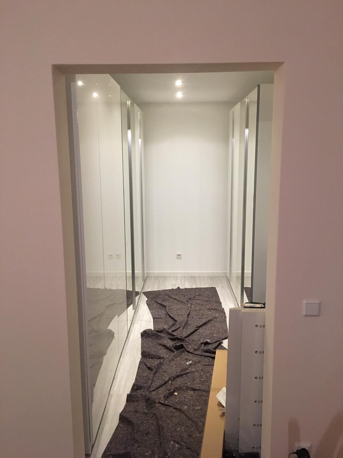 Begehbarer Kleiderschrank mit spiegelnden Schiebetüren, weißem Innenraum und dunklem Teppich.