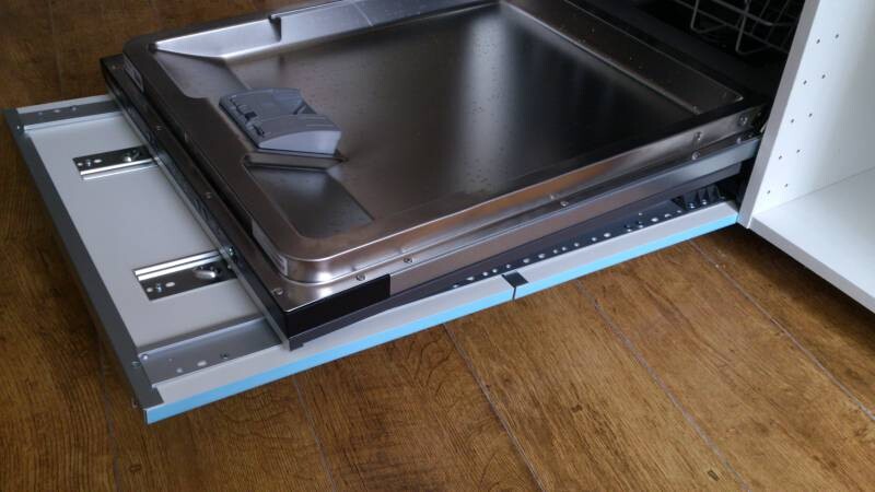 Ausziehbares Edelstahl-Backblech auf Gleitschienen im Küchenschrank; Holzboden sichtbar.