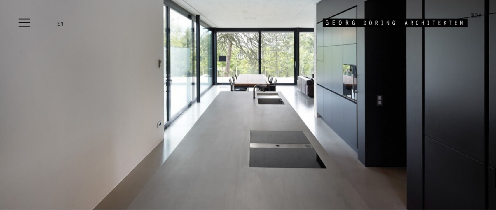 Moderne Küche mit Insel, Induktionsfeld und dunklen Schränken; große Glasfront mit Blick nach draußen