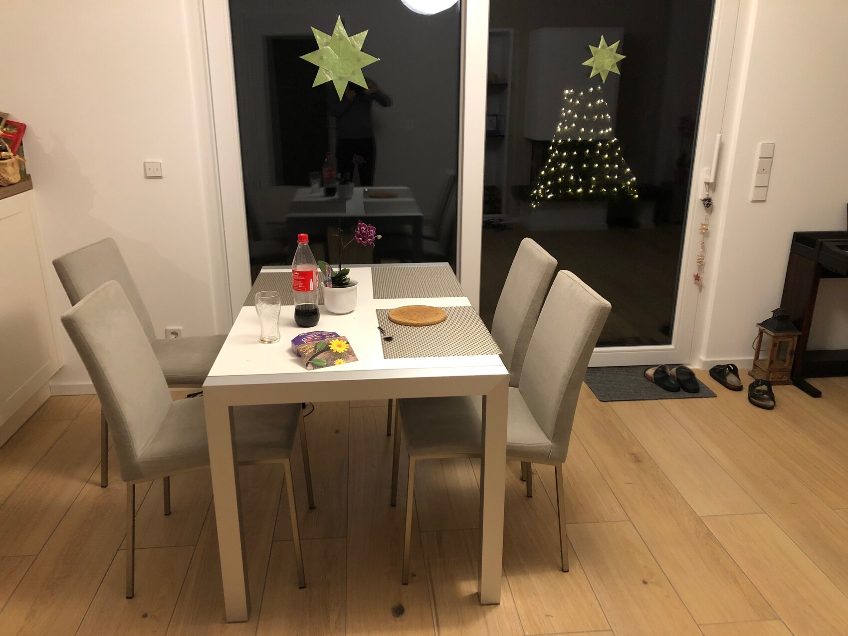Moderner Essbereich mit weissen Tisch und hellgrauen Stuehlen, Glasfront mit Weihnachtsbaum.