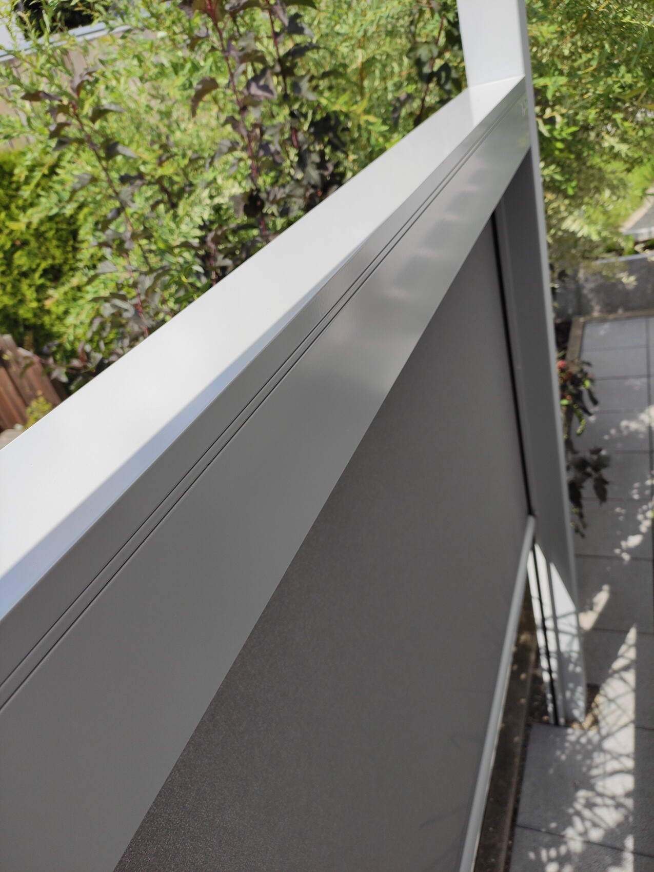 Nahaufnahme eines grauen Metallgeländers an einem Balkon mit grünem Hintergrund.