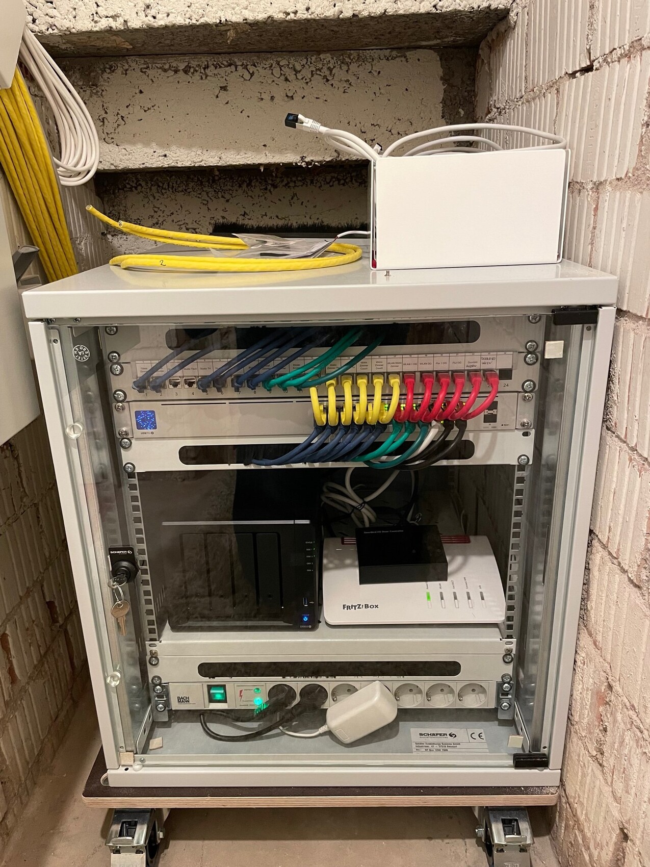 Offener Netzwerkschrank mit Patchpanel, Fritz!Box, NAS und farbigen Kabeln.