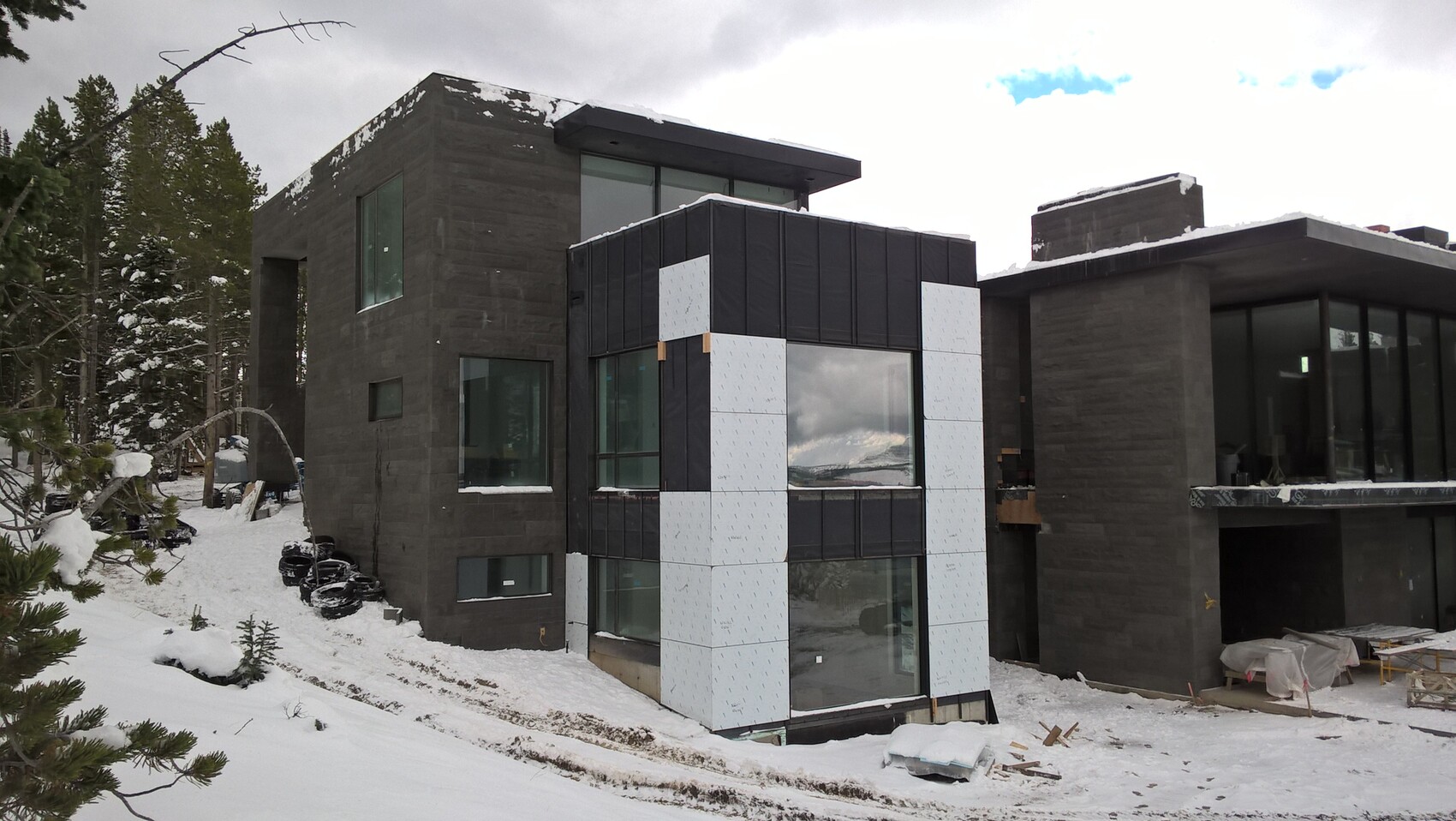 Modernes Haus im Bau im Winter mit dunkler Fassade, großen Fenstern und Schnee.
