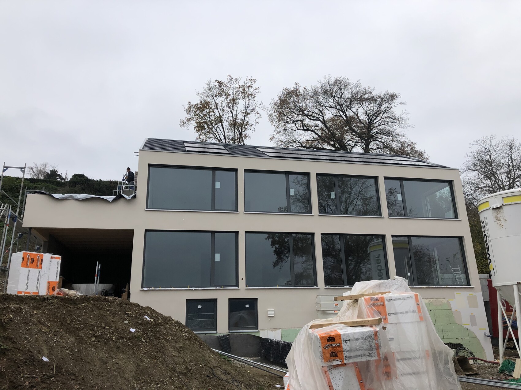 Moderne zweigeschossiges Gebäude mit großen Fensterfronten, Baustelle und Baumaterialien.