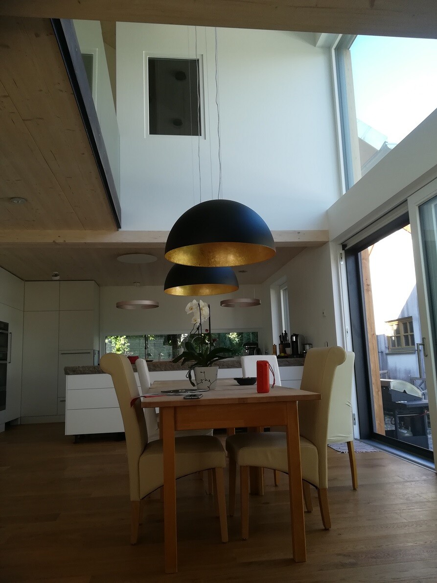 Offener Essbereich: Holztisch, cremefarbene Stühle, Orchidee, schwarze Lampen mit goldener Innenseite