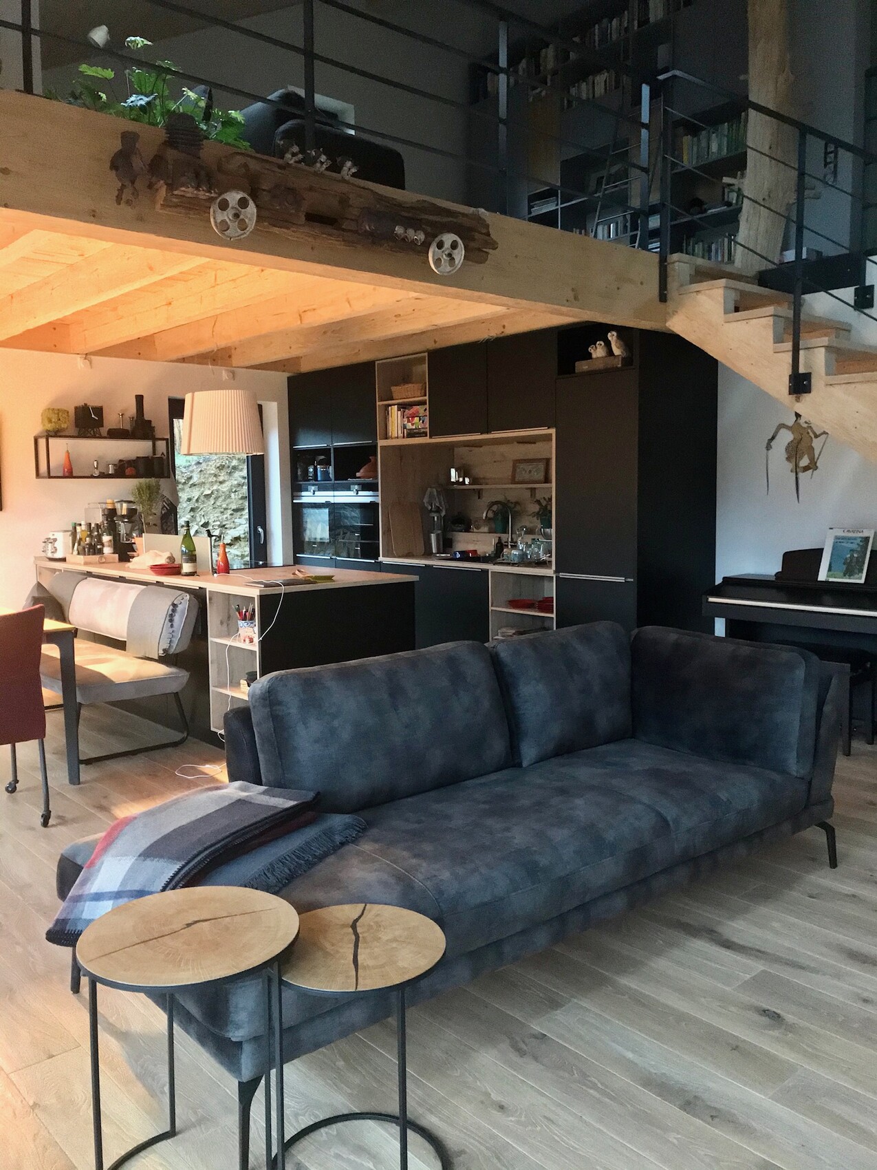Modernes Wohnzimmer mit dunkelblauem Sofa, offener Küche, Holzböden und Loft mit Treppe.