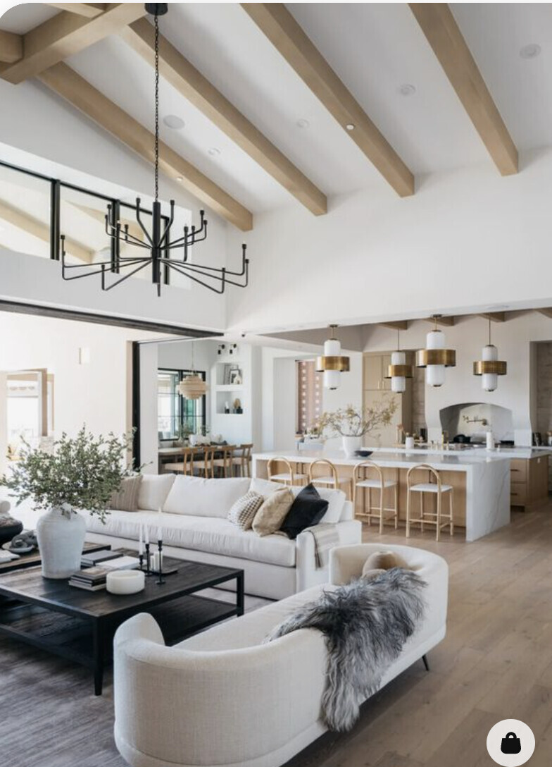 Offener Wohn- und Küchenbereich mit Holzbalkendecke, weißem Sofa, Couchtisch und Insel.