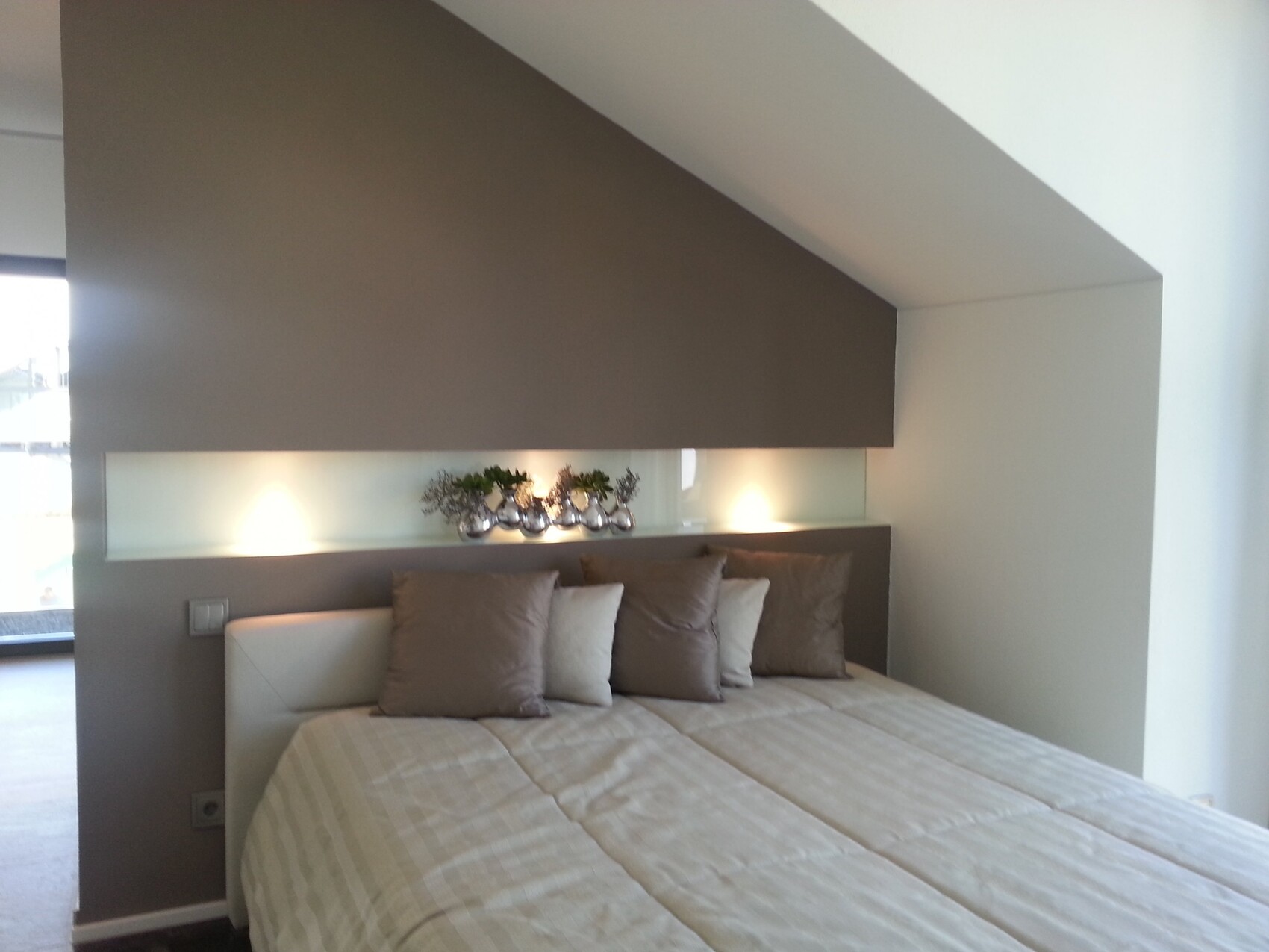 Modernes Schlafzimmer: Bett, beige Decke, Kissen; beleuchtete Glas-Nische hinter Kopfteil.