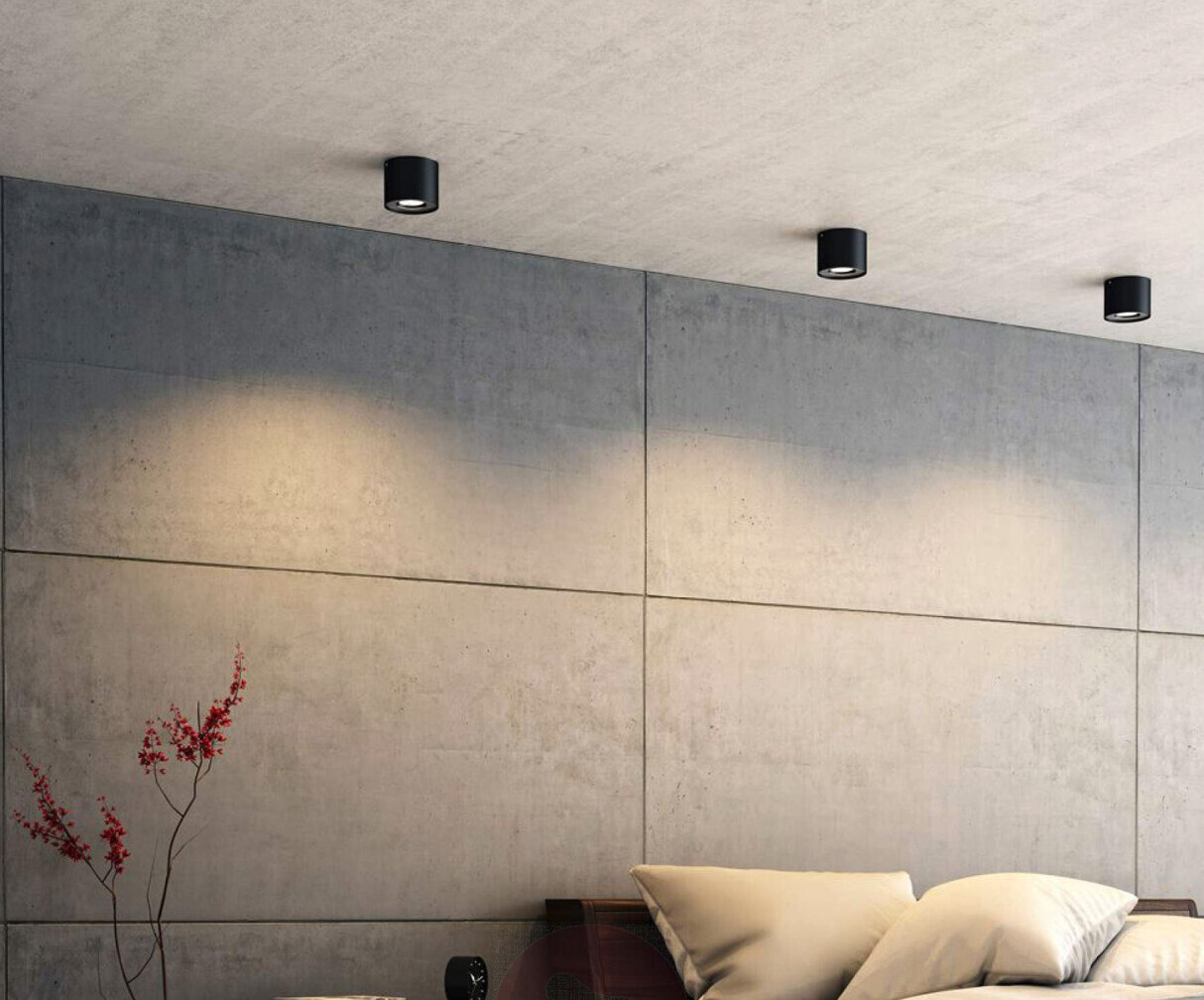 Modernes Schlafzimmer mit Betonplattenwand, Bett, drei Deckenspots und rotem Beerenzweig.