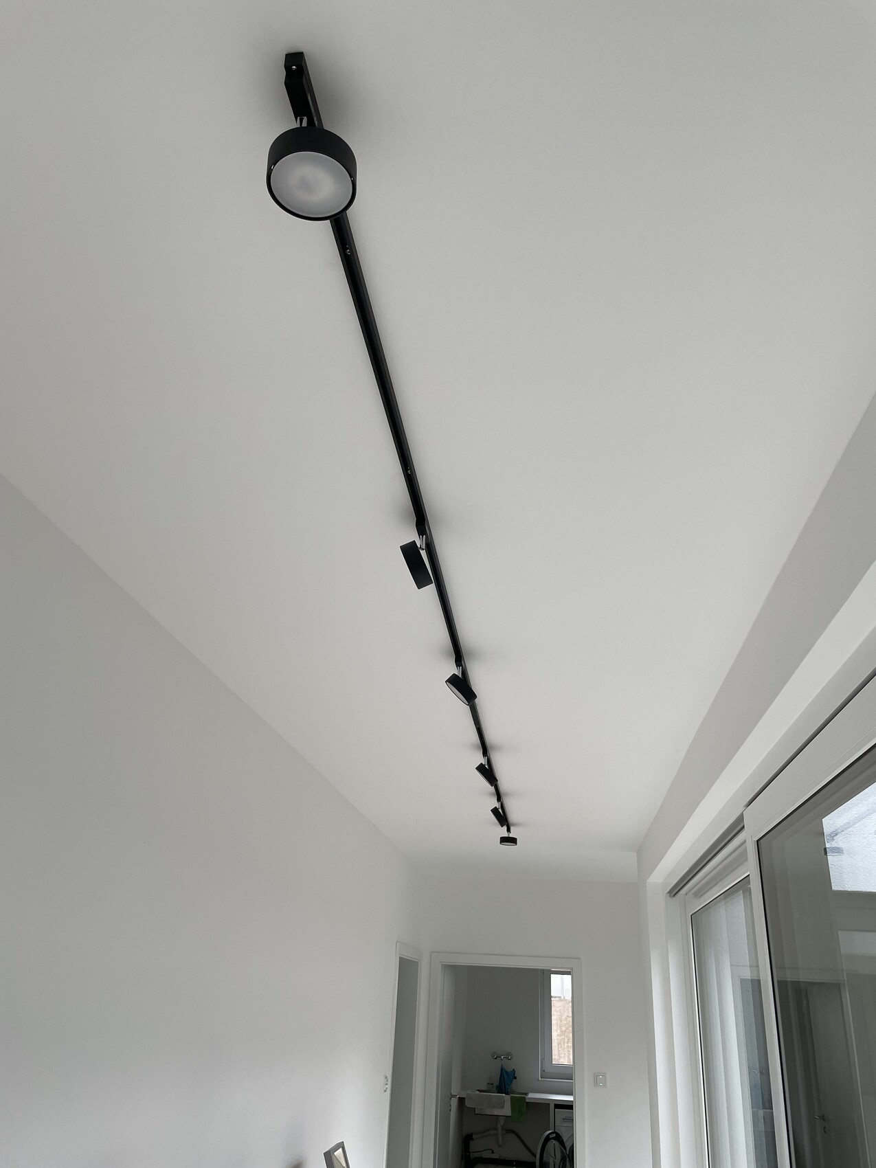 Schwarze Decken-Trackleiste mit mehreren Spots entlang einer weißen Zimmerdecke.