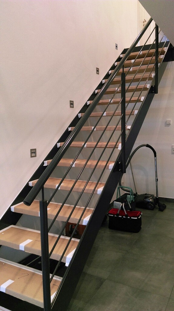 Moderne Innen-Treppe mit schwarzem Metallgeländer, Holzstufen; Staubsauger daneben.
