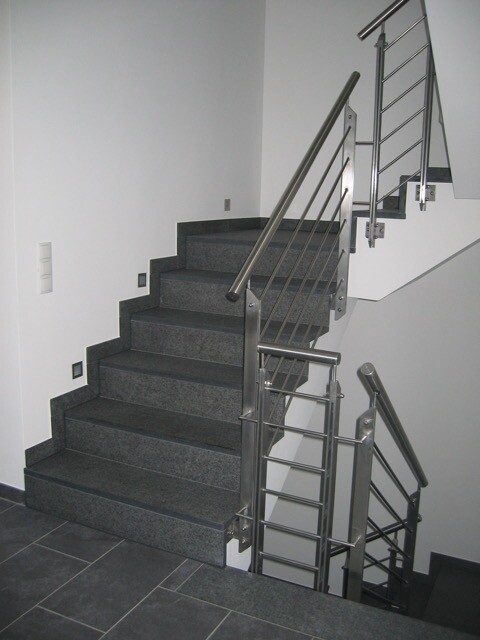 Moderne Innen-Treppe aus dunklem Stein mit Edelstahlgeländern, Blick auf zwei Treppenläufe.