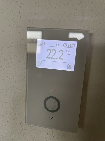 Wandthermostat mit Display zeigt 22.2 °C, Datum und Uhrzeit; runder Knopf darunter.