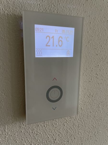 Wand-Thermostat mit Display; zeigt 21.6 °C, Uhrzeit 09:21, Auf/Ab-Tasten.