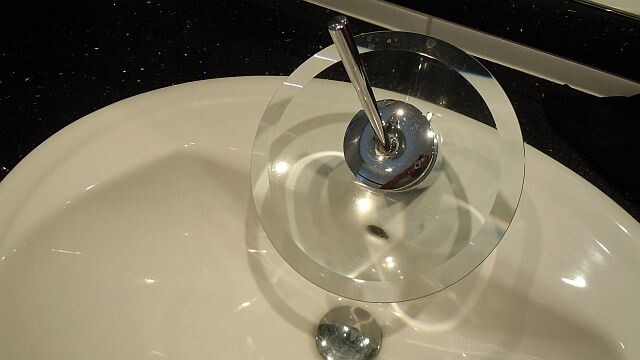 Moderner Waschbecken mit Glasring um den Wasserhahn über dem Becken.
