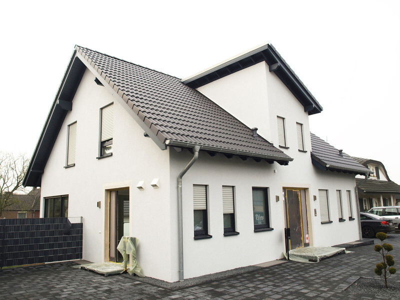 Modernes weißes Einfamilienhaus mit grauem Satteldach, Fensterfronten und gepflasterter Hofeinfahrt