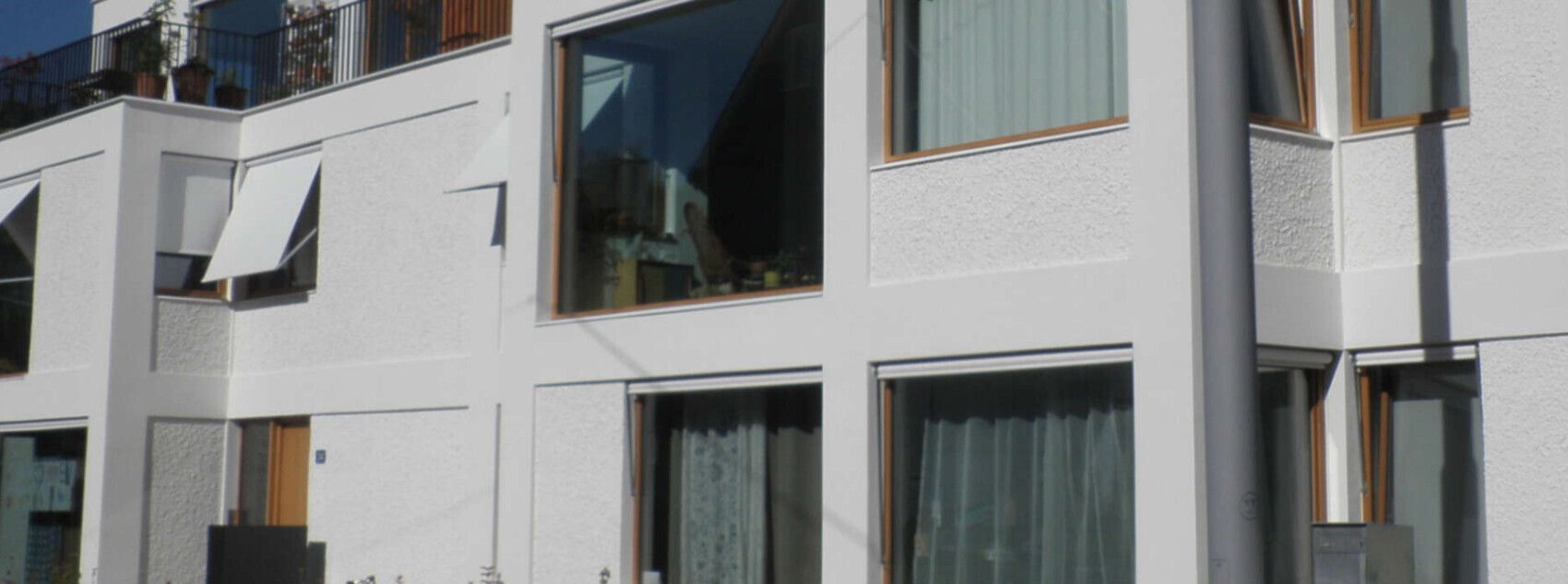 Weiße moderne Wohnhausfassade mit großen Fenstern, Holzrahmen und Balkonpflanzen