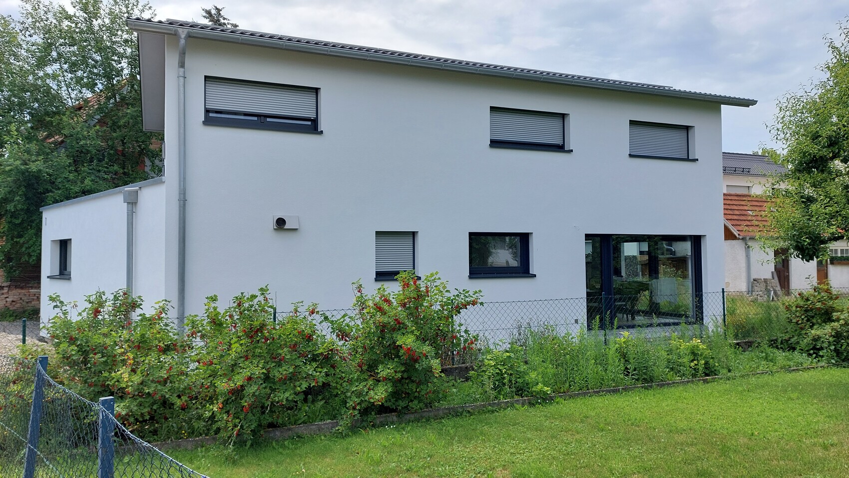 Modernes, weißes zweistöckiges Haus mit großen Fenstern, Garten und Zaun im Vordergrund