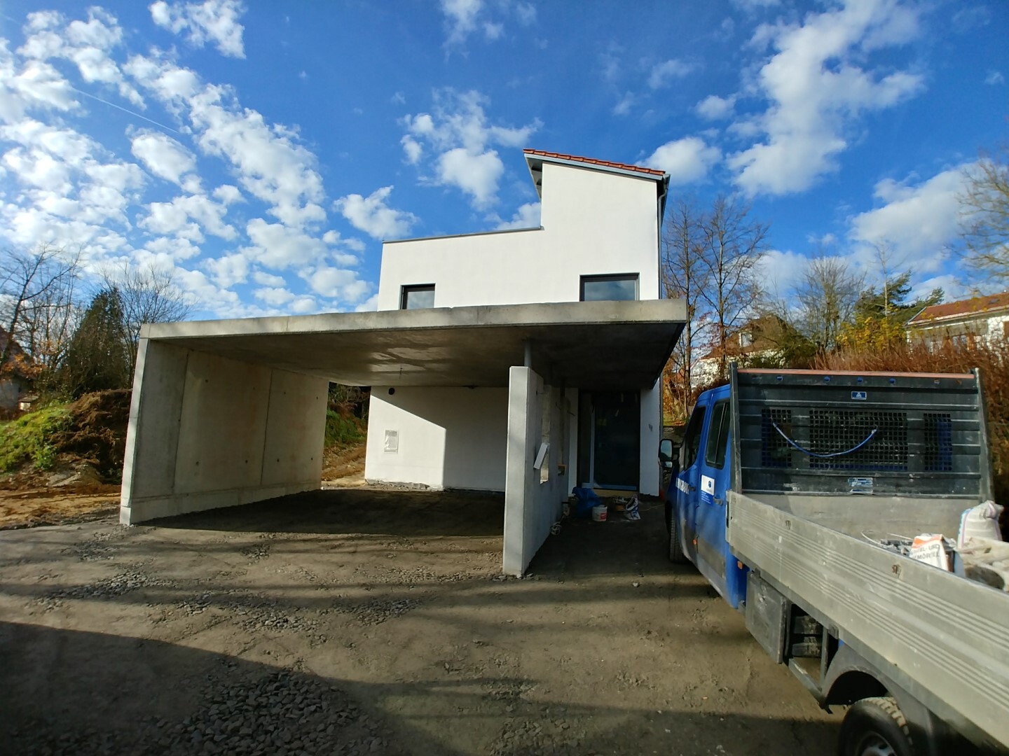 Moderne weiße Hauskonstruktion mit Carport, Bau-LKW daneben, blauer Himmel.