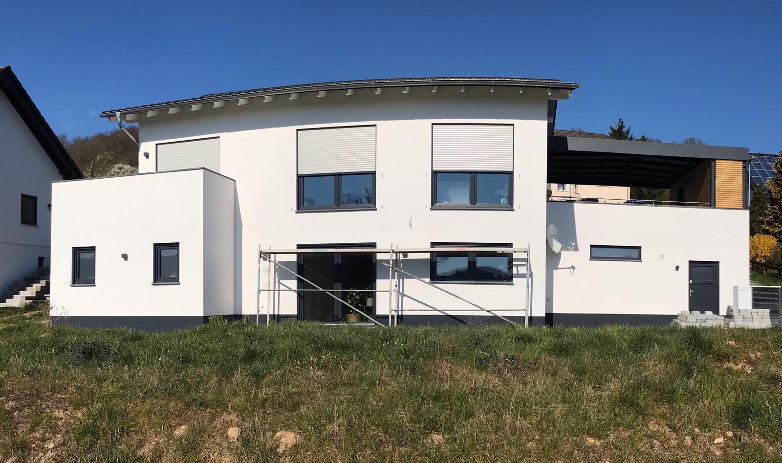 Moderne weiße Hausfront mit großen Fenstern, Baugerüst vor Eingang, grasiger Vorgarten