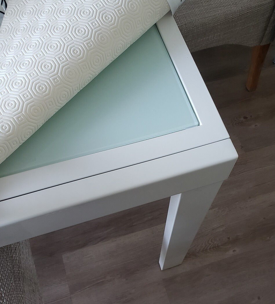 Weißer Tisch mit Glasplatte; darauf ein aufgewickelter, geometrisch gemusterter Stoff.