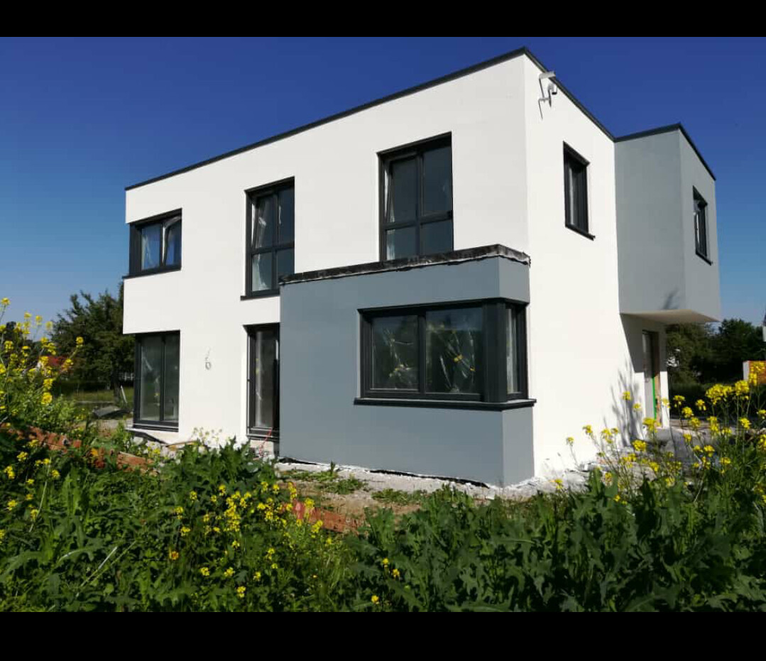 Modernes zweistöckiges Haus mit weißer und grauer Fassade, großen Fenstern, Garten mit Gelbblumen.