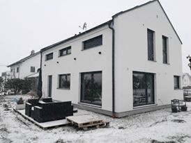Modernes weisses, zweigeschossiges Haus mit großen Fenstern auf schneebedecktem Bauplatz.