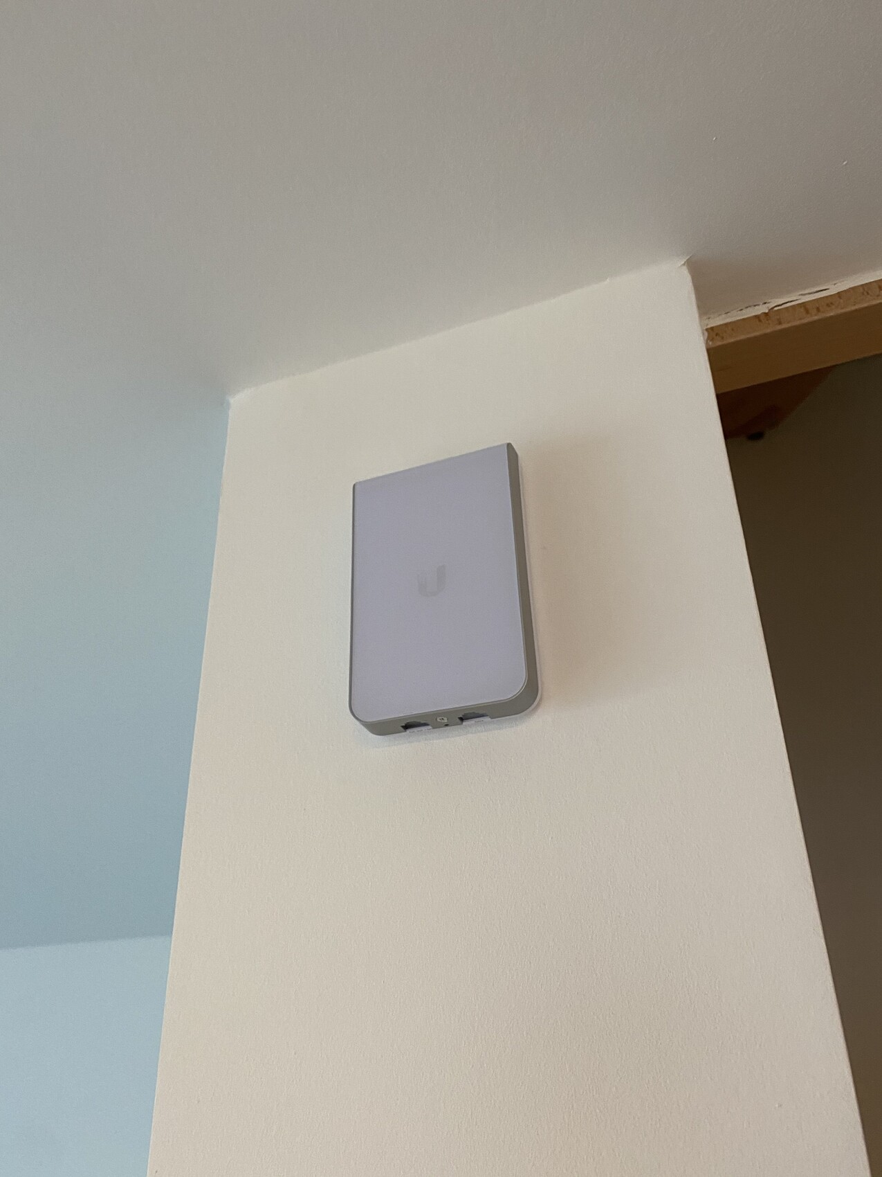 Kleines weißes Wandgerät mit abgerundeten Kanten, vermutlich WLAN-Zugangspunkt, an der Wand montiert.