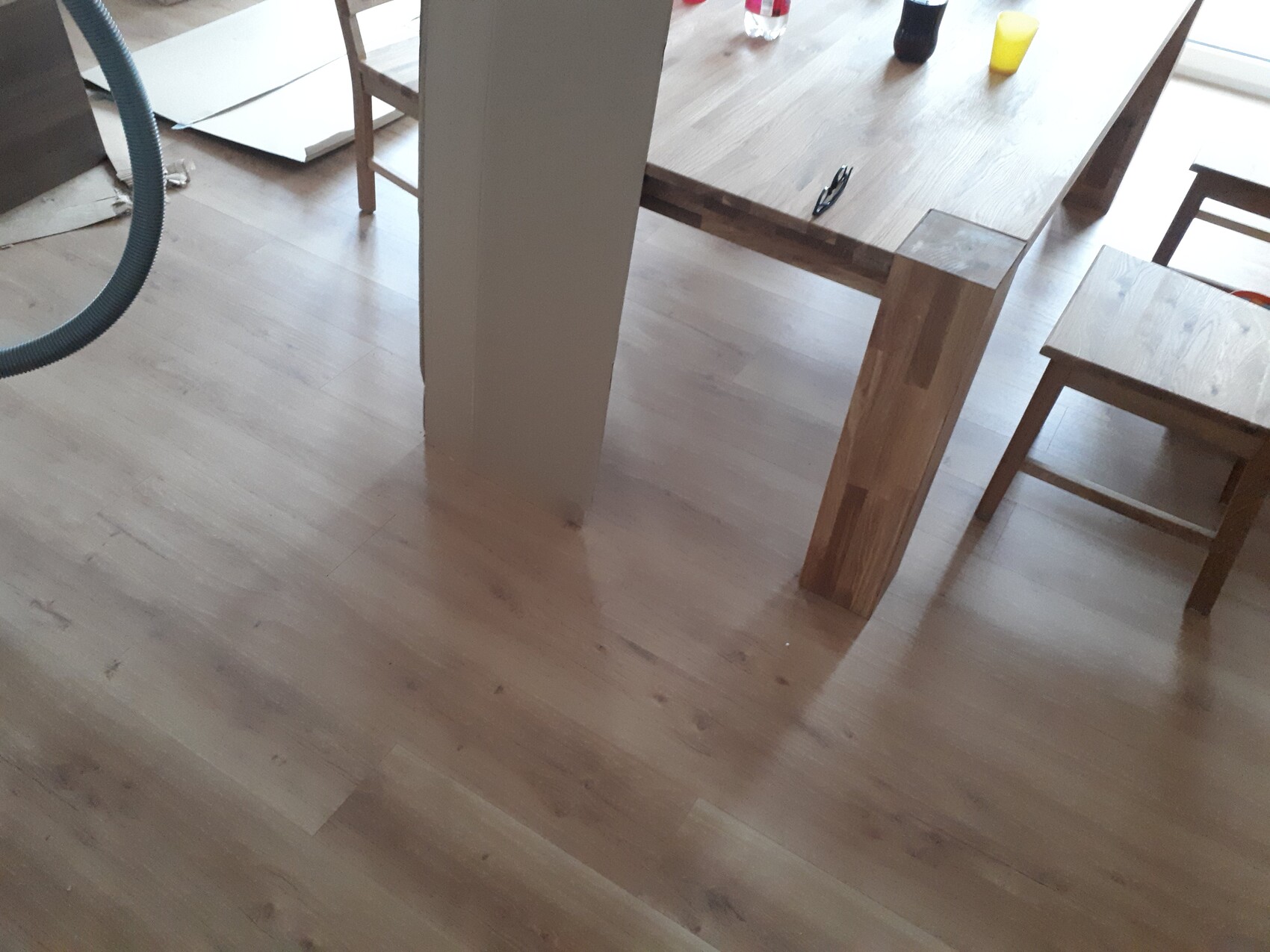Heller Holztisch mit zwei Stühlen, auf dem Tisch Flaschen und Sonnenbrille; Holzfußboden.