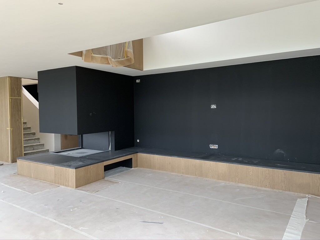 Moderner Wohnzimmerbereich im Bau: schwarze Wand, Kamin, Holzbank und Treppe.