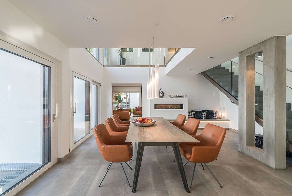 Moderne Ess- und Wohnbereich: langer Holztisch, orange Stühle, Glaswände, Treppe.