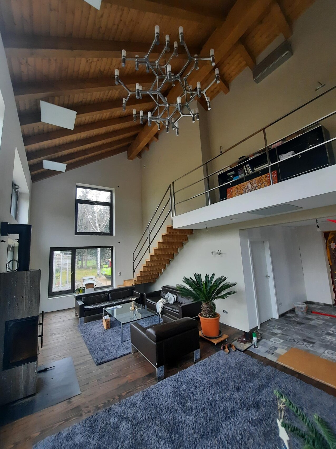 Loft-Wohnzimmer mit Holzbalkendecke, moderner Kronleuchter, Treppe zur Galerie, Ledersofas.