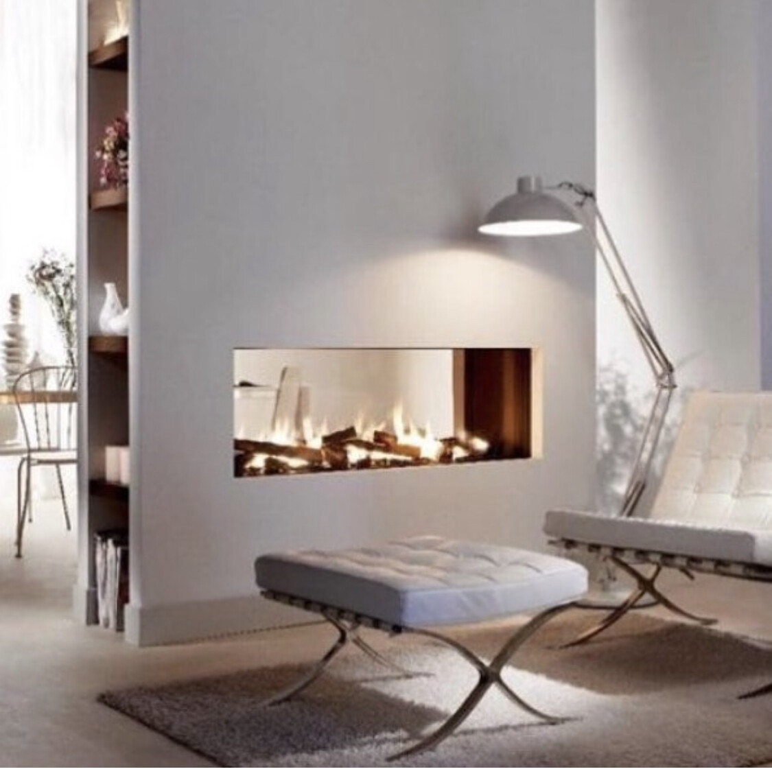 Moderner Wohnraum mit brennendem Wandkamin, weißen Lounge-Sesseln, Fußhocker und Leselampe.