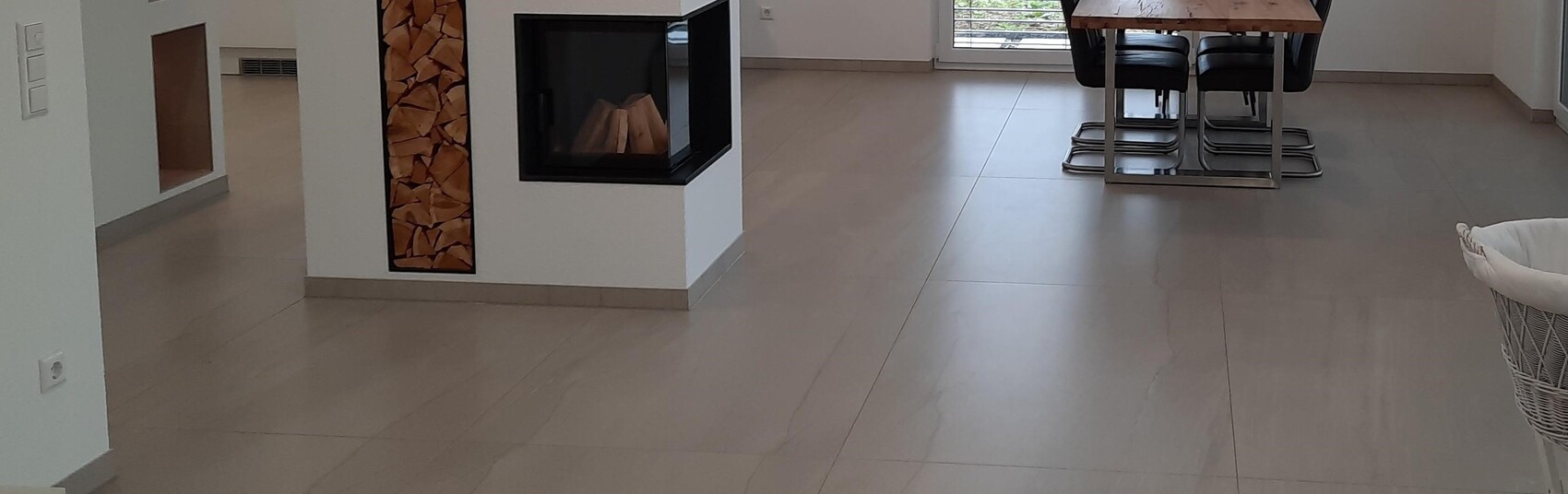 Heller Wohnraum mit eingebautem Kamin, Holzstapel in Nische, Esstisch und Stühle im Hintergrund