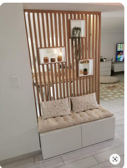 Weiße Sitzbank mit gepolsterten Kissen vor einer Holz-Lattenwand mit Nischen und Pflanzen.