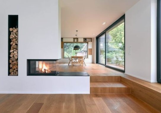 Moderner Wohnbereich mit Kamin, Holzfußboden, Treppenstufen und großen Glasfenstern.