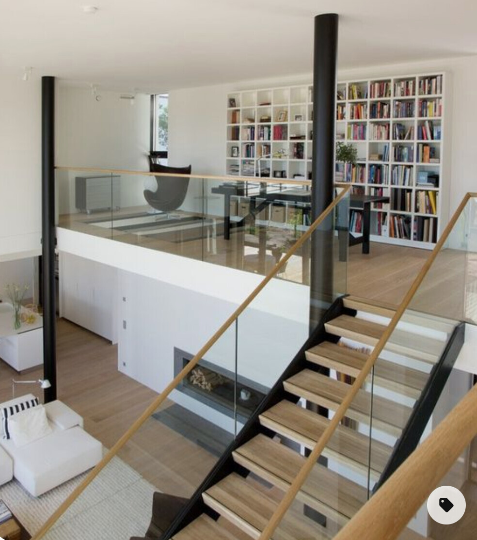 Moderne Loftwohnung mit Glasgeländer, Treppe und großer Bücherwand im Arbeitsbereich.