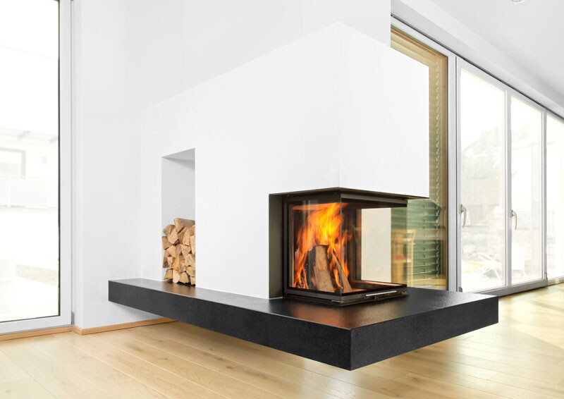 Moderne weiße Kaminanlage mit Holzvorrat links, Feuer hinter Glasfront, große Fenster dahinter