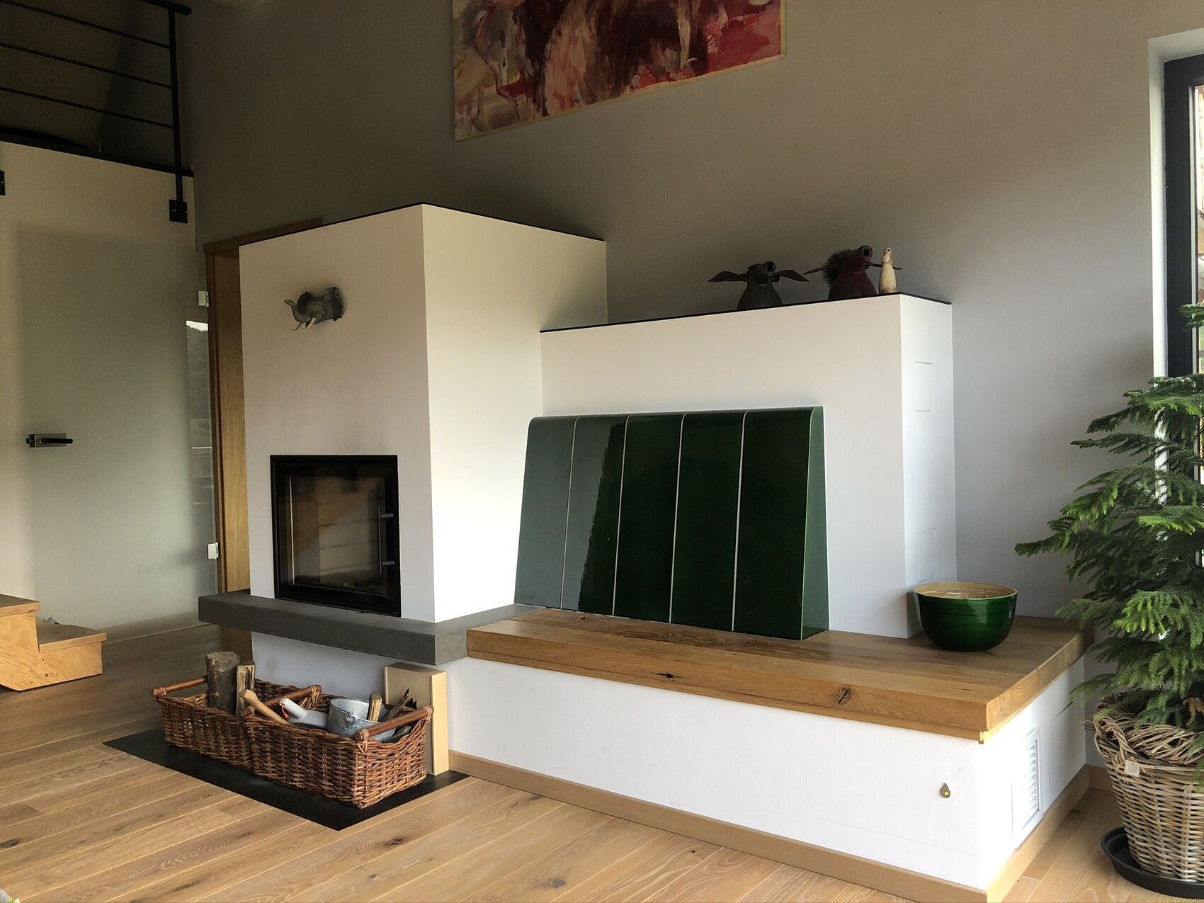 Moderner Wohnraum mit Kamin in einer weißen Wandnische, Brennholzkorb und grüne Paneele.